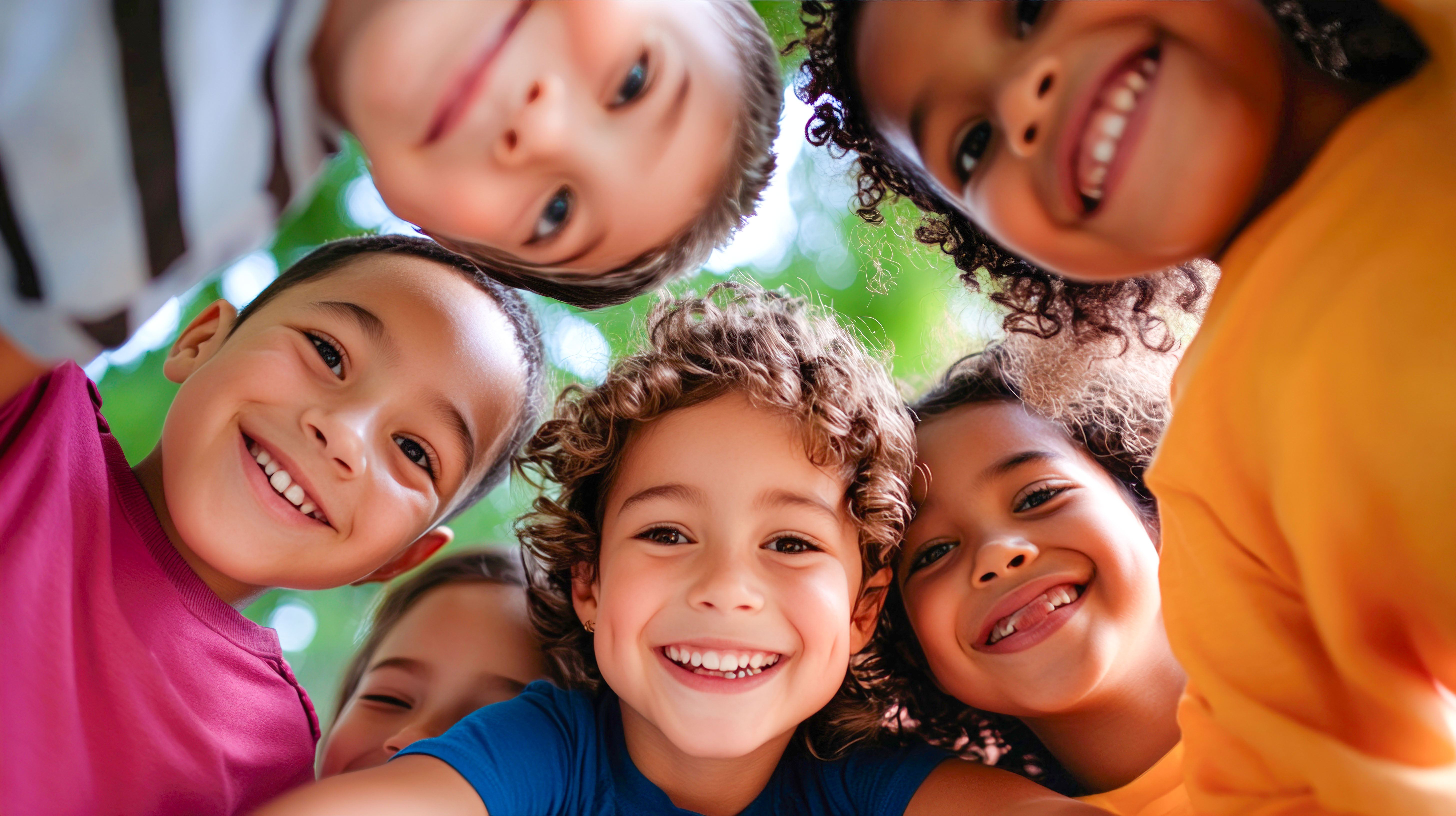 Diverse children in a huddle smiling joyfully with green outdoor background